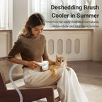 Woman using a deshedding brush cooler on a cat in a room with a window.